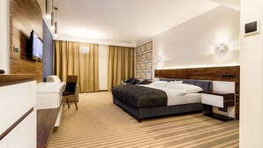 A modern hotel room with a large bed, a desk, and a TV mounted on the wall.