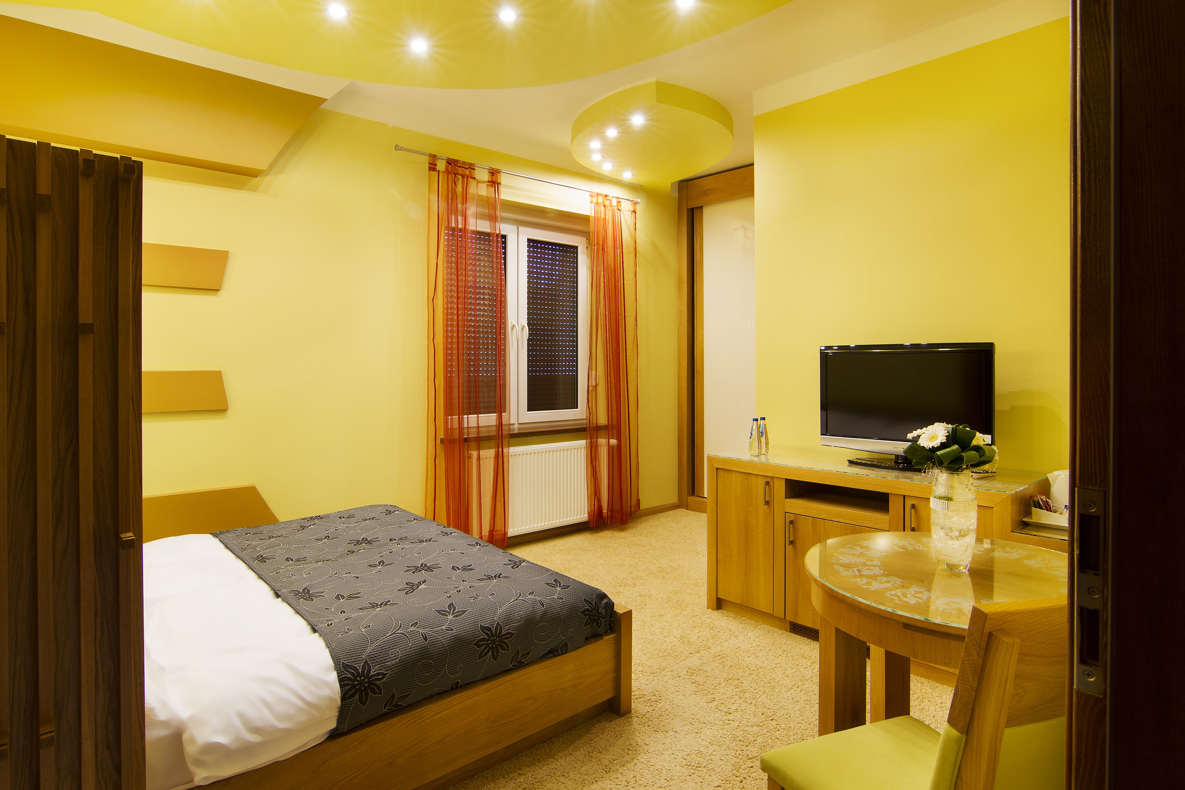 A bedroom with a bed, a desk with a television, a chair, and a window with curtains.