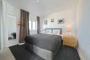 Une chambre d’hôtel moderne avec un grand lit, des tables de chevet, une armoire et une fenêtre avec des rideaux.