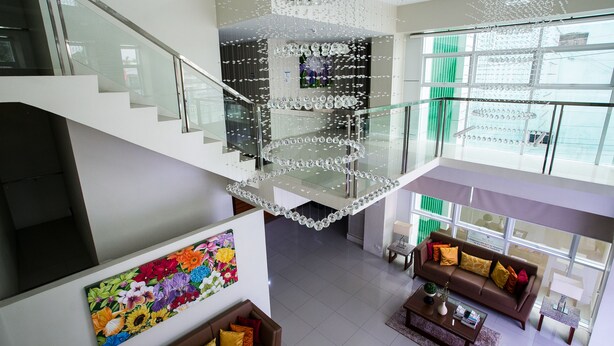 Ein geräumiger Innenraum mit moderner Treppe, Glastrennwand, einem farbenfrohen Blumenbild, einem braunen Sofa mit Kissen und einem großen Fenster mit Aussicht.