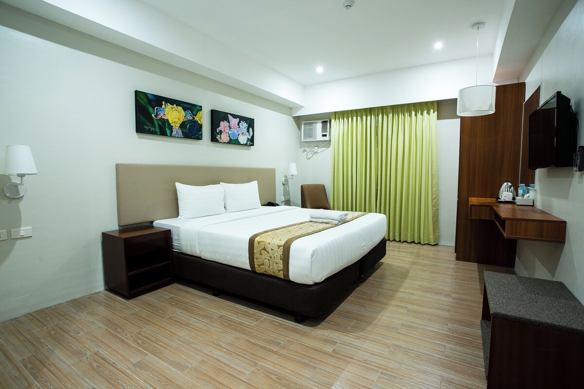 Une chambre d’hôtel avec un grand lit, des tables de chevet, un bureau, une chaise, une télévision et des œuvres d’art accrochées au mur.
