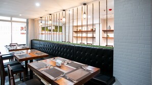 Ein Restaurant mit langen Gemeinschaftstischen, schwarzen gepolsterten Sitzgelegenheiten und hängenden Pendelleuchten.