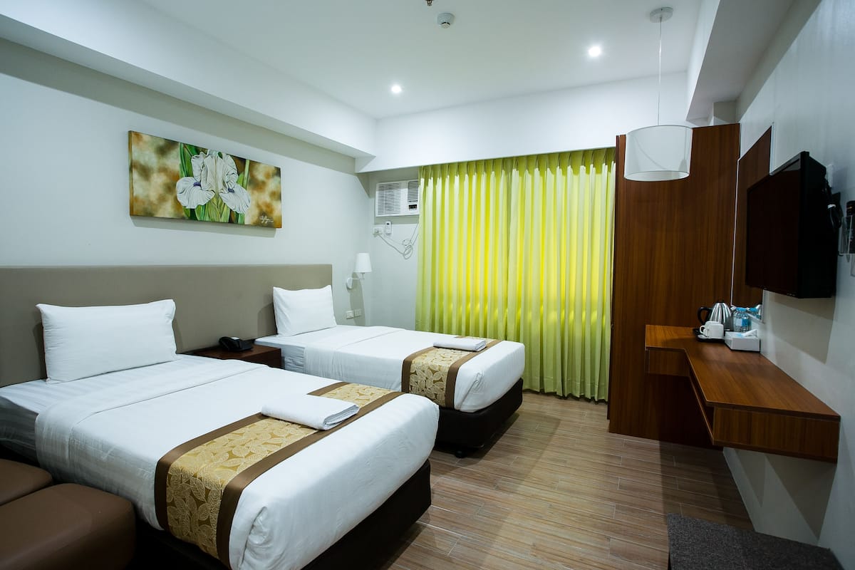 Ein Hotelzimmer mit zwei Betten, einem Schreibtisch, einem Fernseher und einem Bild an der Wand.
