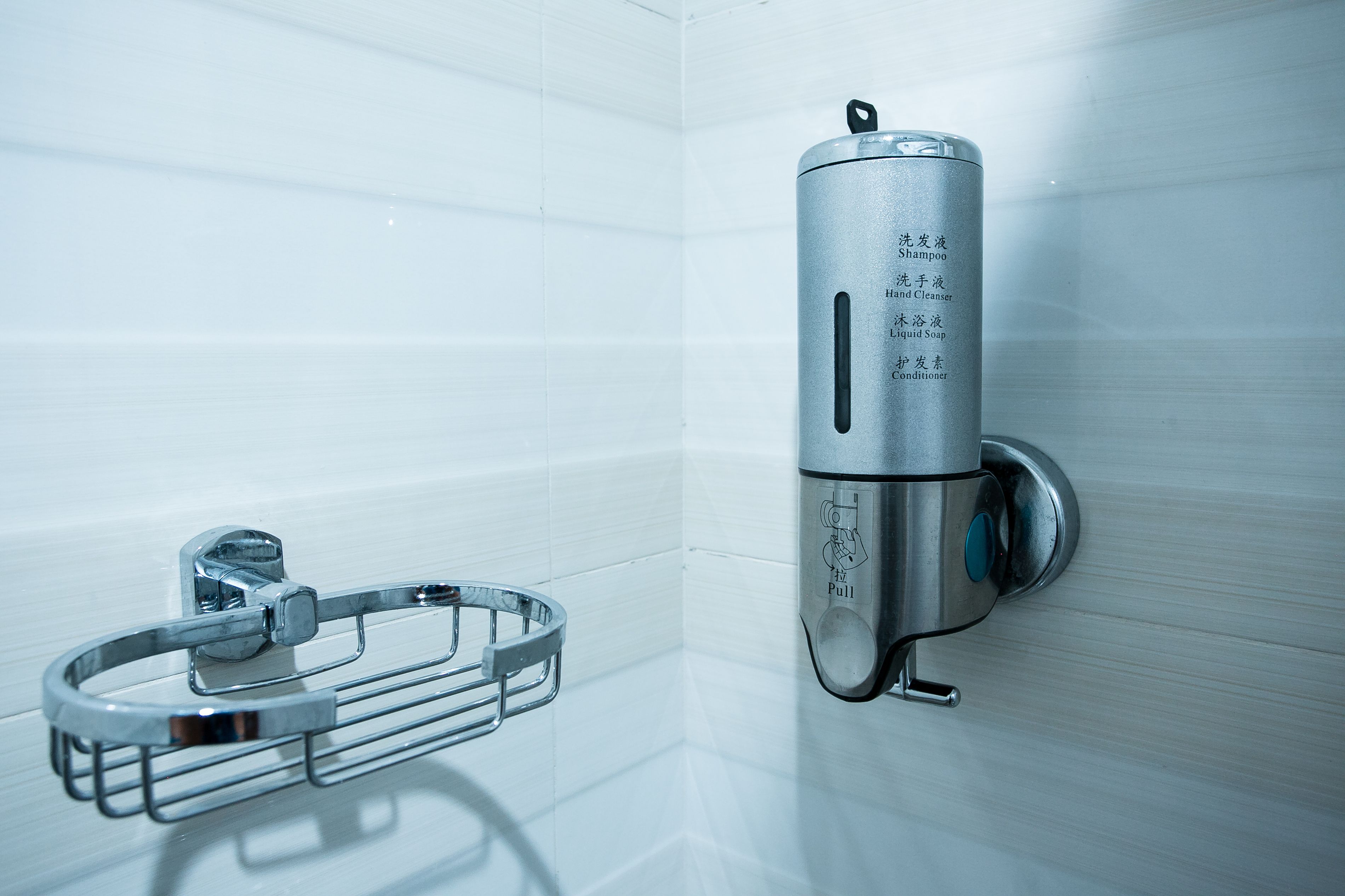 A bathroom with a wall-mounted soap dispenser and a metal towel rack.