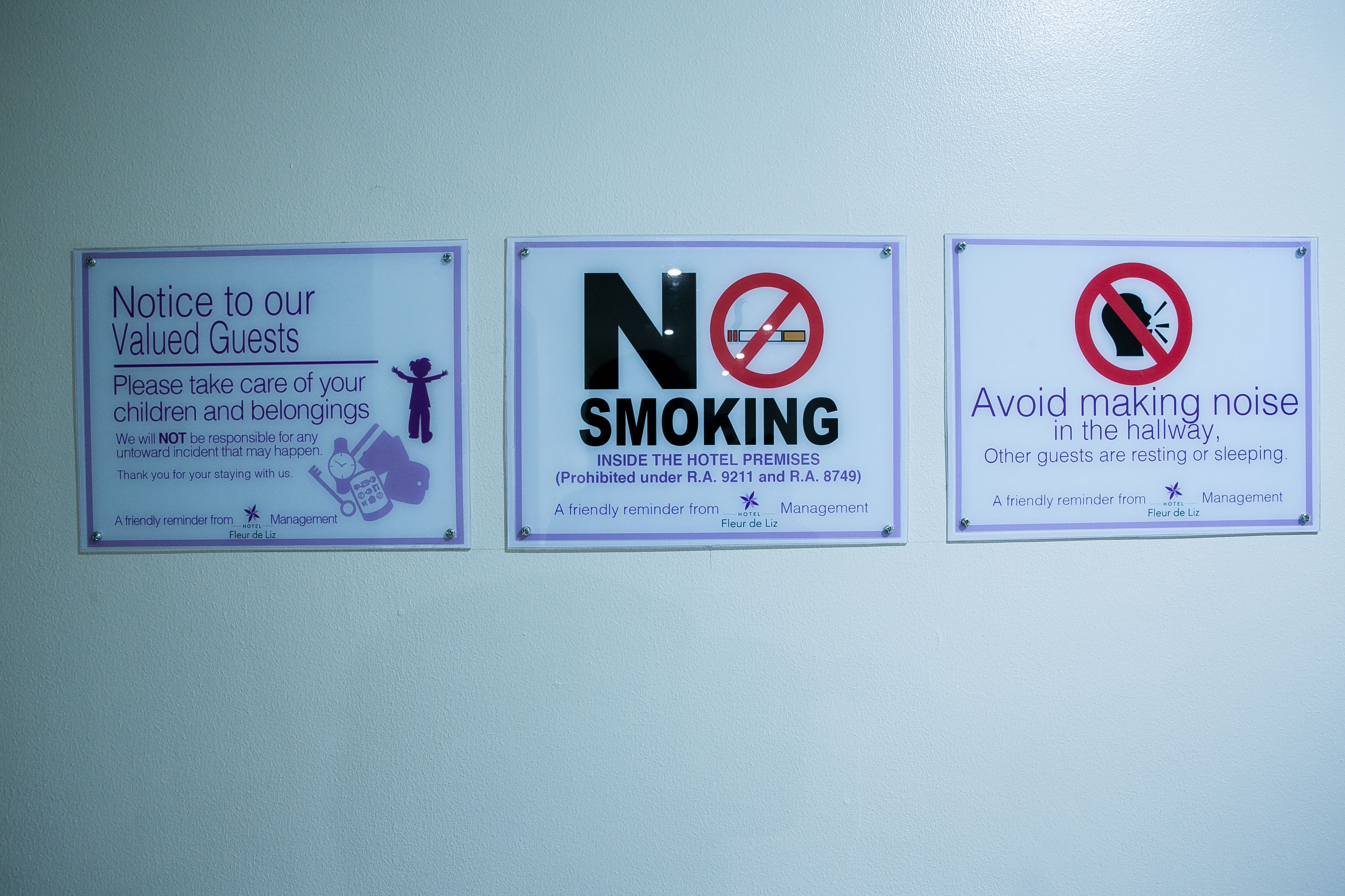 Tres letreros en una pared: un aviso para los huéspedes sobre el cuidado de sus pertenencias, un letrero de no fumar y una indicación para que los huéspedes eviten hacer ruido en el pasillo.
