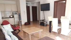 Un salon comprenant un canapé, une table basse, un téléviseur et un coin repas avec des chaises.