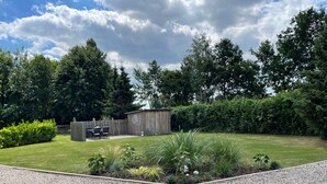 A well-maintained garden with a wooden shed, a gravel path, and a seating area with chairs and a table. - cozy apartment in the Bay of Lübeck (Neuenhagen)