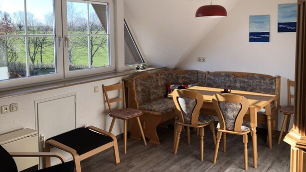 A dining area with a wooden table and chairs, a bench, and a view of the outdoors through a window. - cozy apartment in the Bay of Lübeck (Neuenhagen)