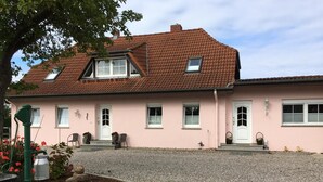 A two-story house with a pink facade, a sloped roof, and a gravel driveway. - cozy apartment in the Bay of Lübeck (Neuenhagen)