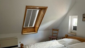 A bedroom with a sloped ceiling, a wooden bed, a small table, and a window. - cozy apartment in the Bay of Lübeck (Neuenhagen)