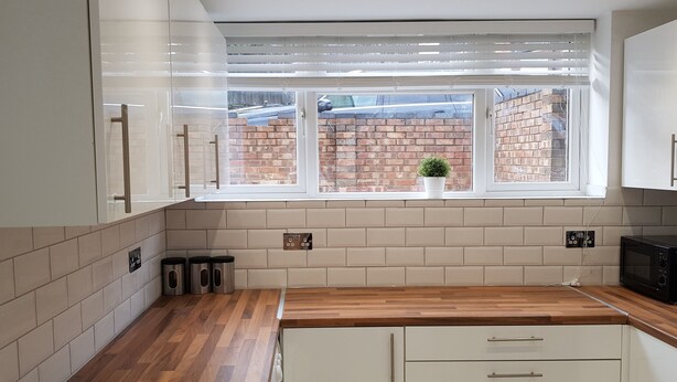 Una cucina moderna con mobili bianchi, un piano di lavoro in legno e una parete in mattoni visibile dalla finestra.