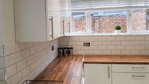 Una cucina moderna con mobili bianchi, un piano di lavoro in legno e una finestra che si affaccia su un muro in mattoni.