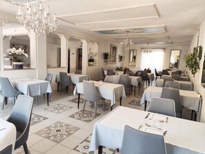 A dining area with multiple tables and chairs, chandeliers, and decorative mirrors. - Hôtel Restaurant Le Commerce (Nogaro)