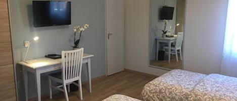 Een slaapkamer met twee bedden, een bureau met stoel, een aan de muur bevestigde televisie en een spiegel die de kamer weerspiegelt.