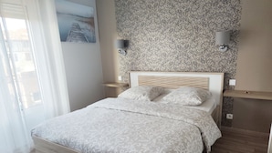 A bedroom with a wooden bed, patterned bedding, a wall-mounted lamp, and a decorative wall hanging. - Hôtel Restaurant Le Commerce (Nogaro)