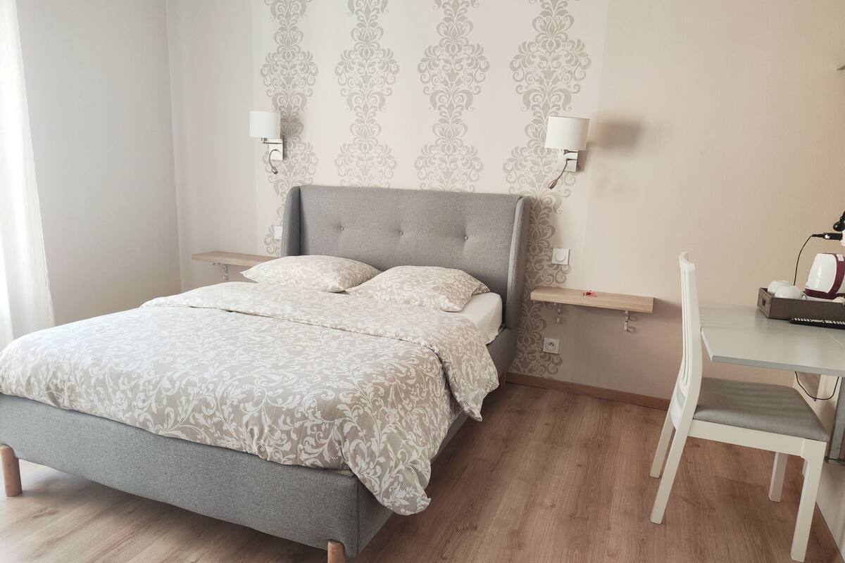 Un dormitorio ordenado con cama, mesitas de noche, un escritorio y una silla.