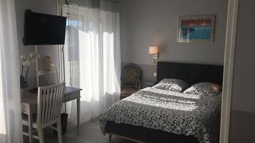 A bedroom with a bed, a desk, a chair, a TV, and a lamp.