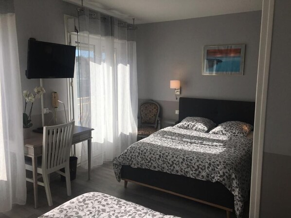 Un dormitorio con cama, escritorio, silla, televisor y lámpara.