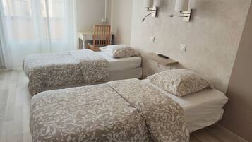 A hotel room with two beds, a nightstand, and wall-mounted lamps.