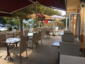 An outdoor cafe with tables and chairs, a fountain, and umbrellas providing shade. - Hôtel Restaurant Le Commerce (Nogaro)