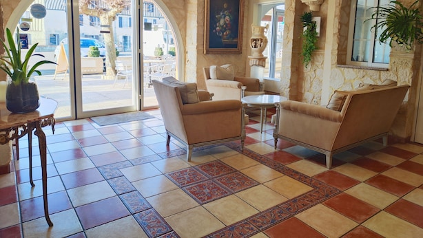 A lobby with a checkered floor, two sofas, a small table, and a large window with a plant. - Hôtel Restaurant Le Commerce (Nogaro)