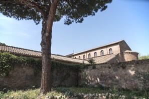 A historic building with a tiled roof, brick walls, and a large tree in the foreground. - BePlace Aventino (Rome)