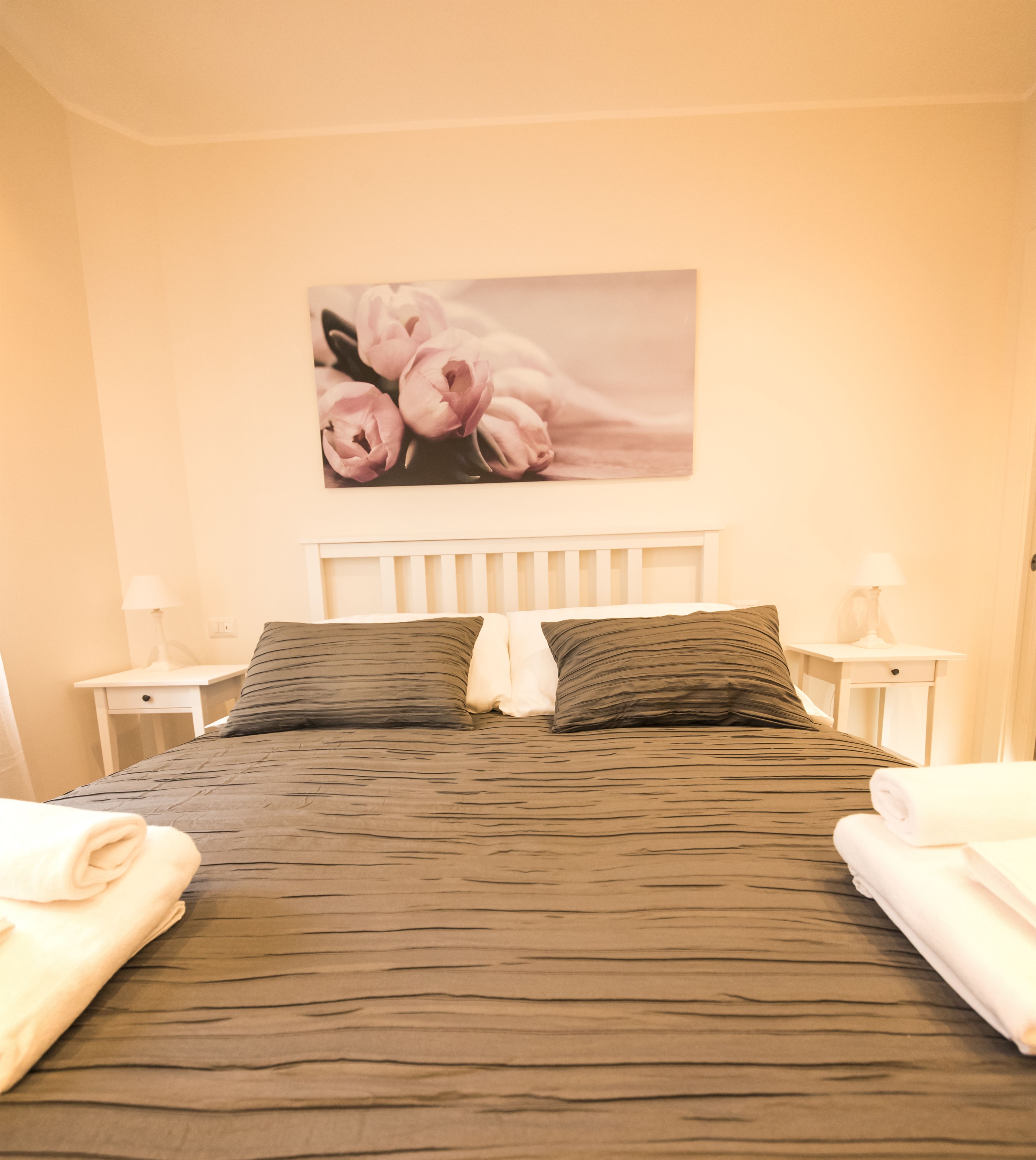A neatly made bed with a dark patterned bedspread, two pillows, and a wall-mounted picture of flowers.