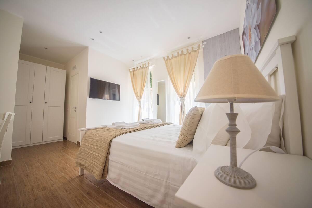 A hotel room with a bed, a bedside table, a lamp, a TV, and a wardrobe.