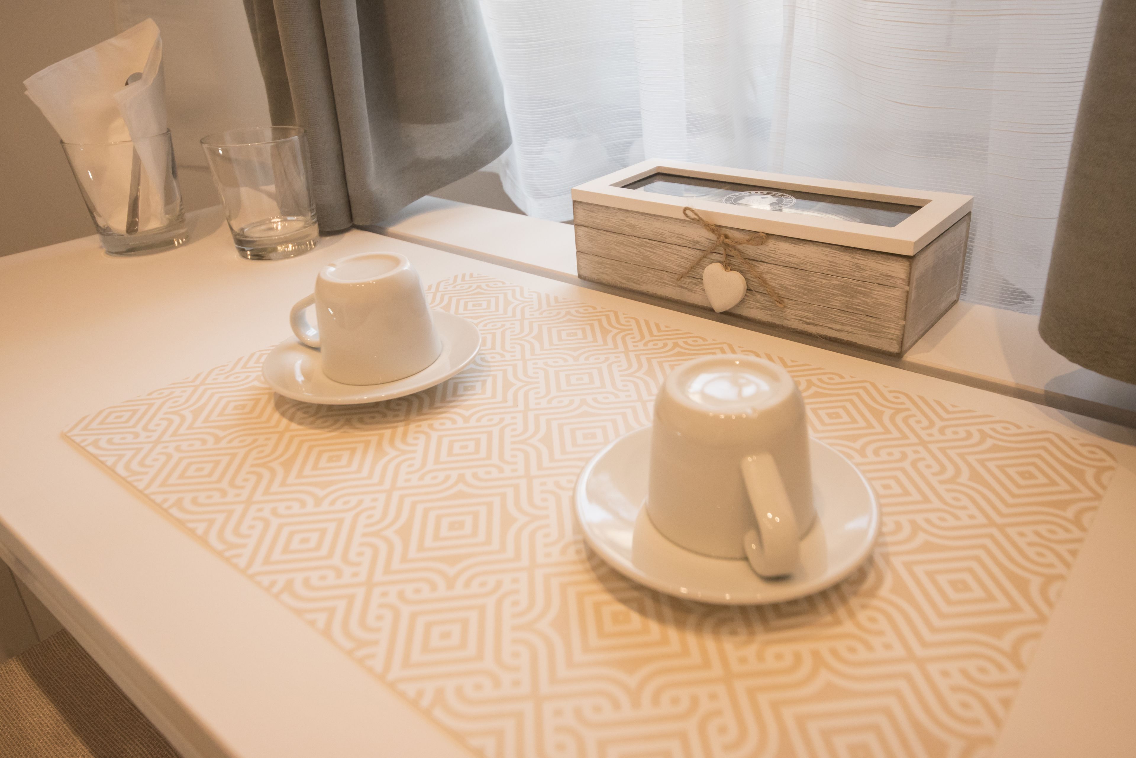 A neatly arranged breakfast table with two white cups and saucers, a small wooden box with a heart-shaped decoration, and a tissue box.