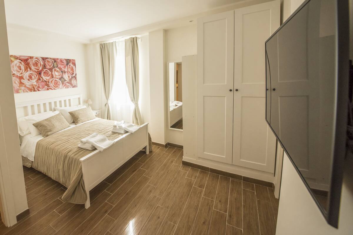 A bedroom with a bed, a wardrobe, a television, and a painting on the wall.