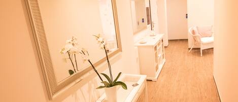 A clean, well-lit hallway with a reception desk, a mirror, and a potted orchid.