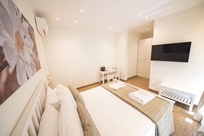 A hotel room with a bed, a desk, a chair, a TV, and an air conditioning unit. - BePlace Aventino (Rome)