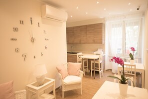 A modern kitchen with wooden cabinets, a dining area with white furniture, and a wall clock. - BePlace Aventino (Rome)