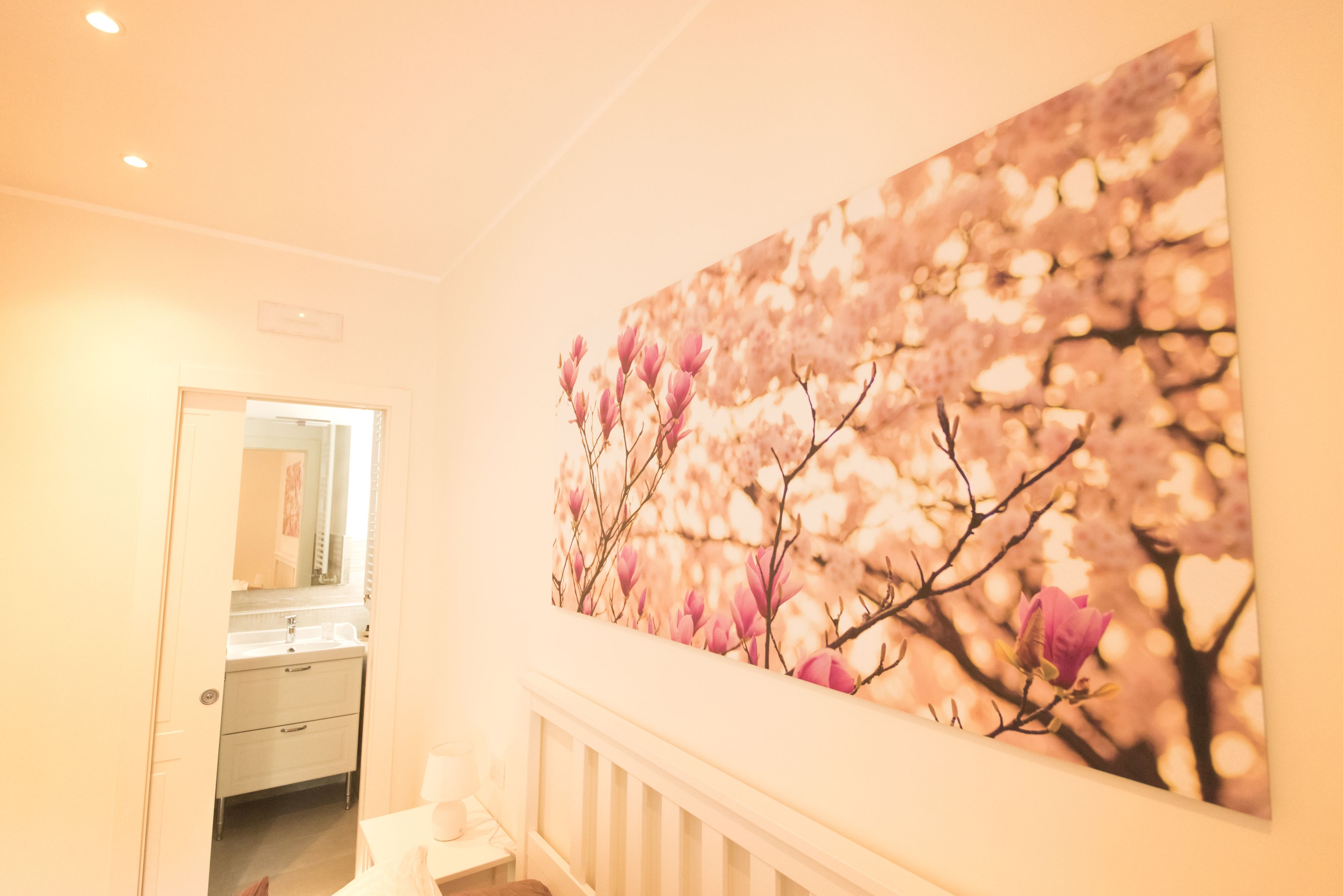 A hallway with a large floral artwork on the wall, a mirror, and a door leading to a bathroom.