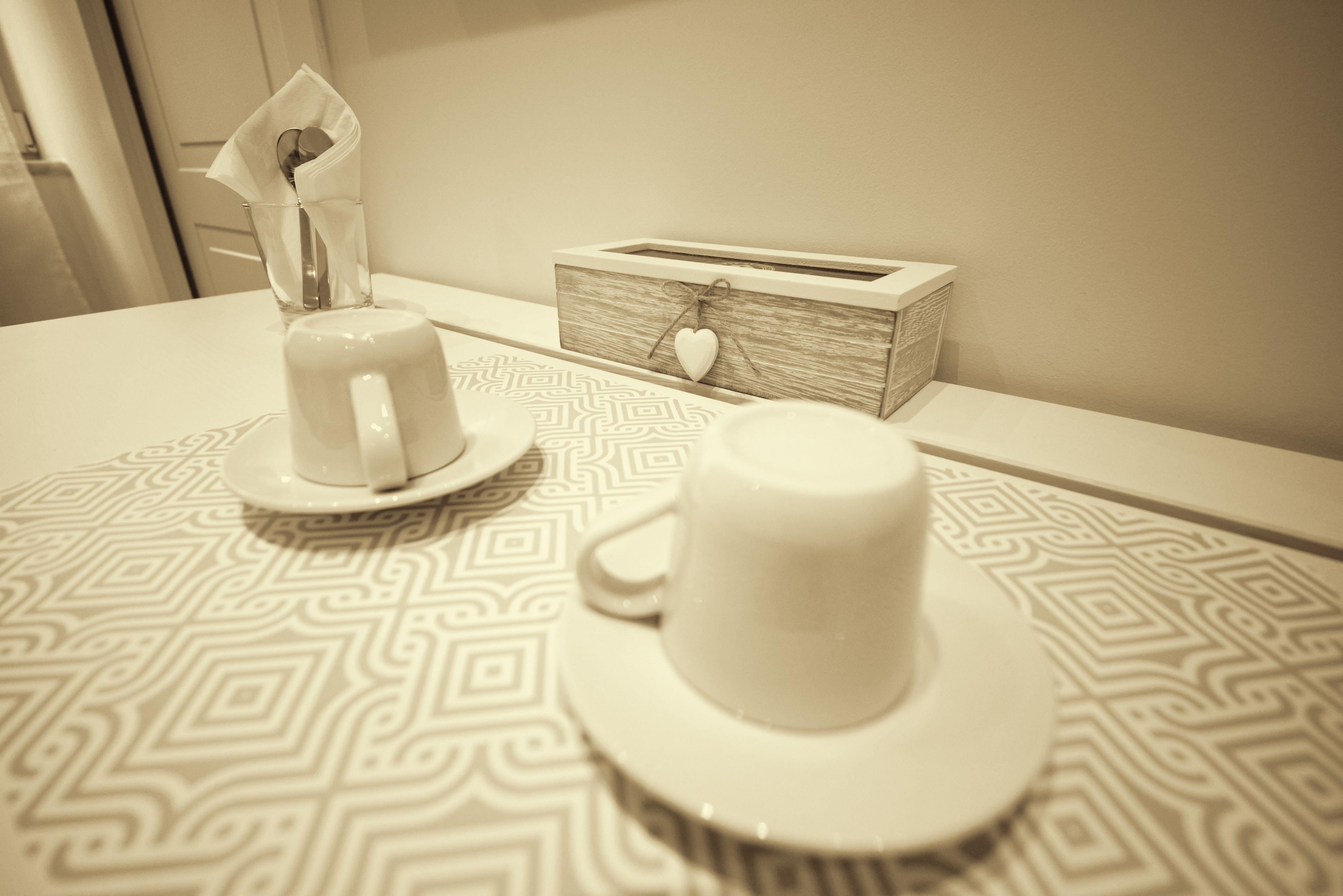 Een tafel met een witte mok en een witte theekop op een tafelkleed met een patroon.