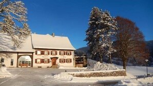 A two-story building with a snow-covered roof and a stone foundation. - Hotel - Landgasthof zum Pflug (Steinen)