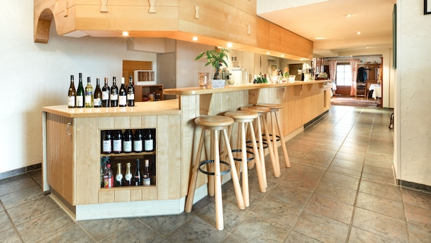 A bar area with wooden stools, a wine display, and a potted plant. - Hotel - Landgasthof zum Pflug (Steinen)