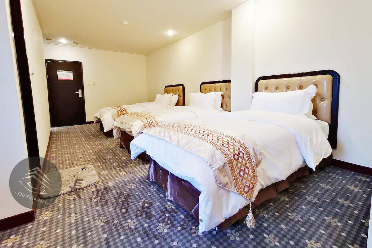 Ein Hotelzimmer mit drei Betten, Teppichboden und einer Tür.