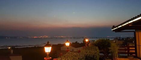 A coastal view at dusk with street lamps and a distant bridge.