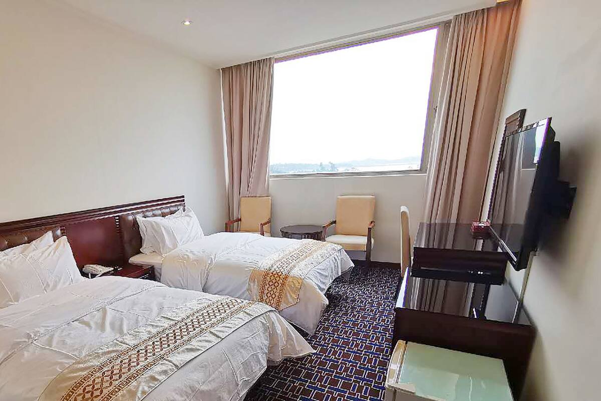 Ein Hotelzimmer mit zwei Betten, einem Schreibtisch, einem Stuhl, einem Fernseher und einem Fenster mit Vorhängen.