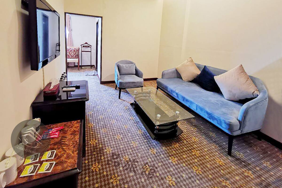 Ein Hotelzimmer mit Sofa, Sessel, Couchtisch, Fernseher und einem kleinen Tisch mit Gegenständen.