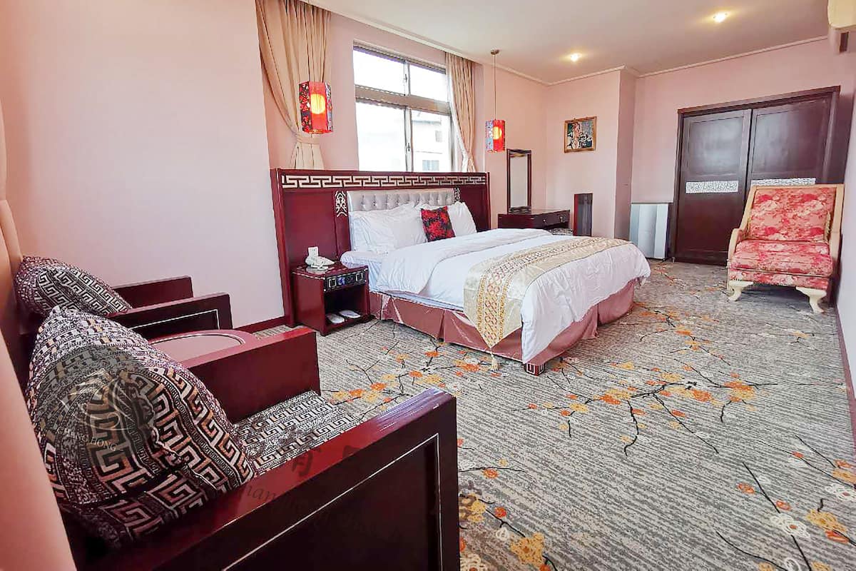 Ein Hotelzimmer mit einem großen Bett, einem Sofa, einem Sessel, einem Nachttisch, einer Kommode und einem Fenster mit Vorhängen.