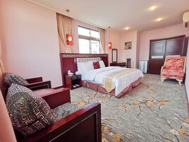 Habitación de hotel con una cama grande, un sofá, una silla, una mesita de noche, un aparador y una ventana con cortinas.