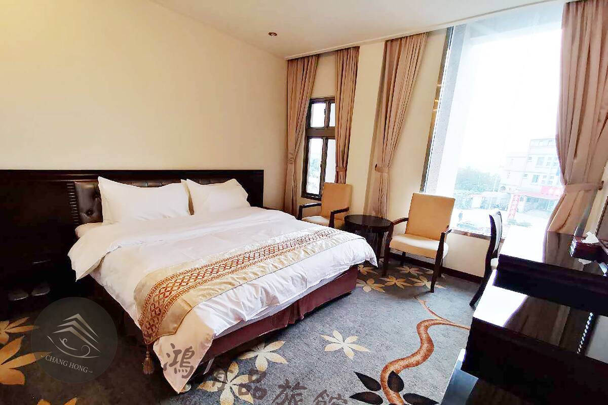 Ein Hotelzimmer mit einem großen Bett, einem Schreibtisch, einem Sessel und Blick auf die Stadt.