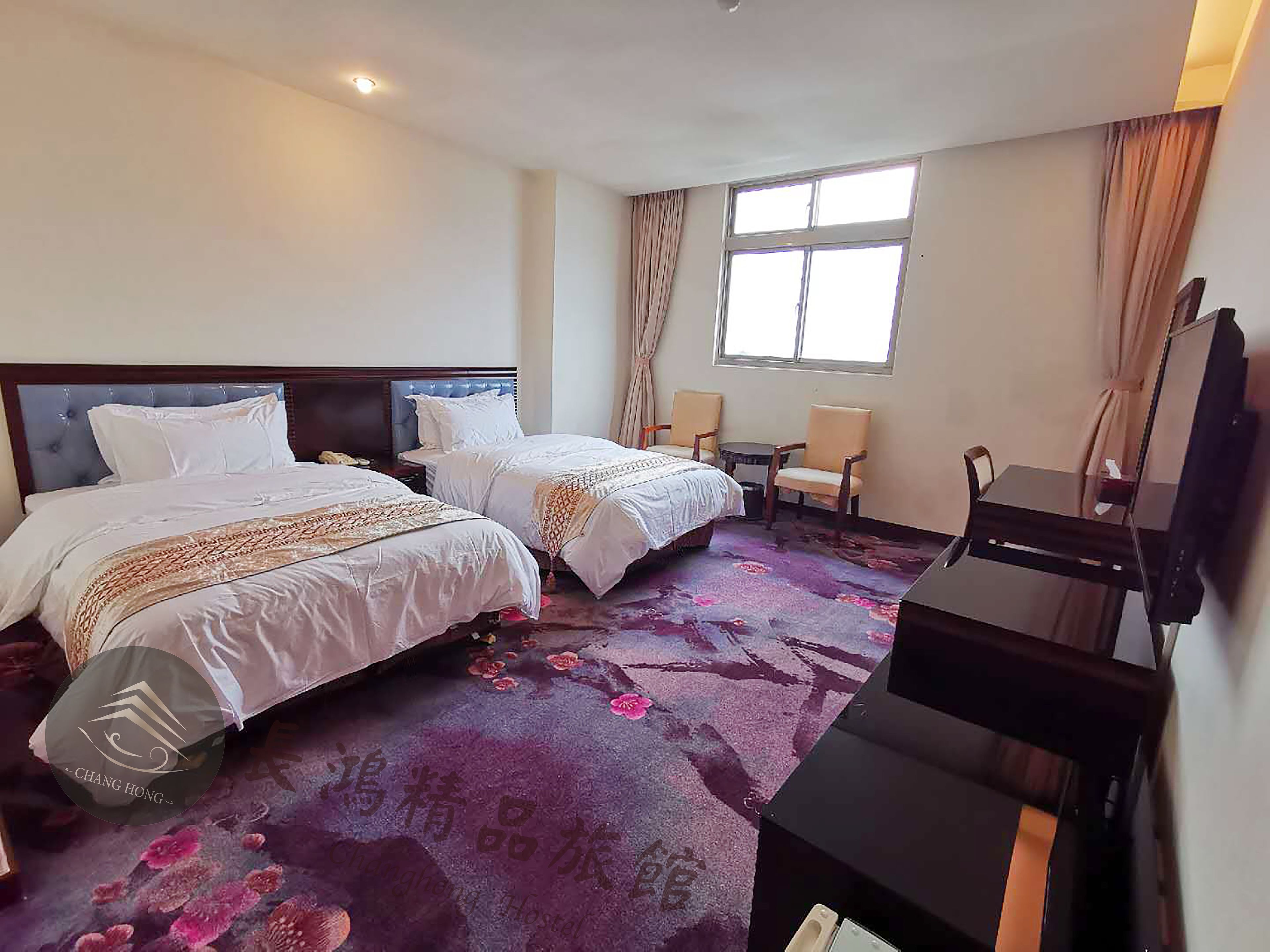 Habitación de hotel con dos camas, un escritorio, una silla, un televisor y una ventana con cortinas.