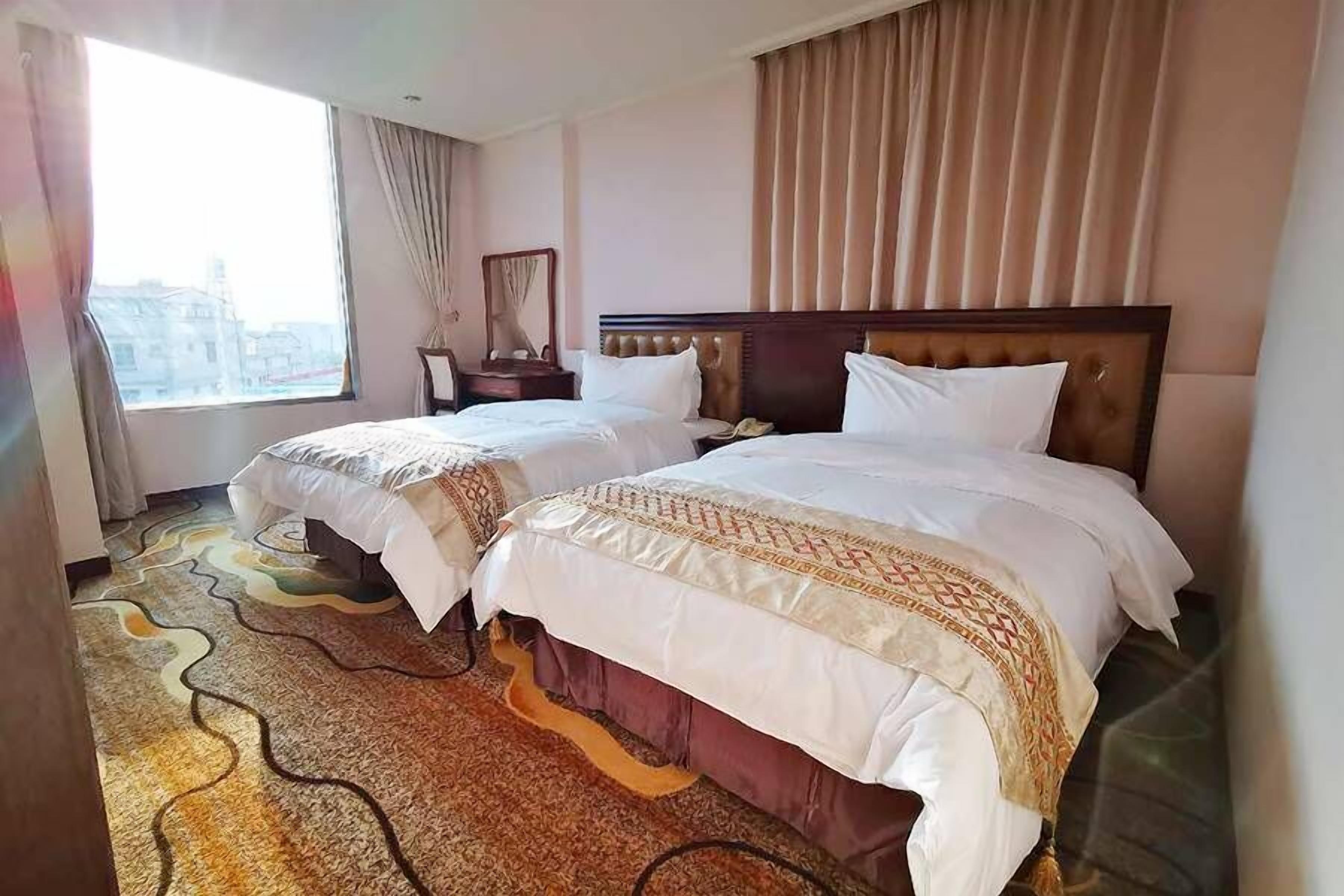 Une chambre d’hôtel avec deux lits, une grande fenêtre, une vue sur la ville et une moquette à motifs.