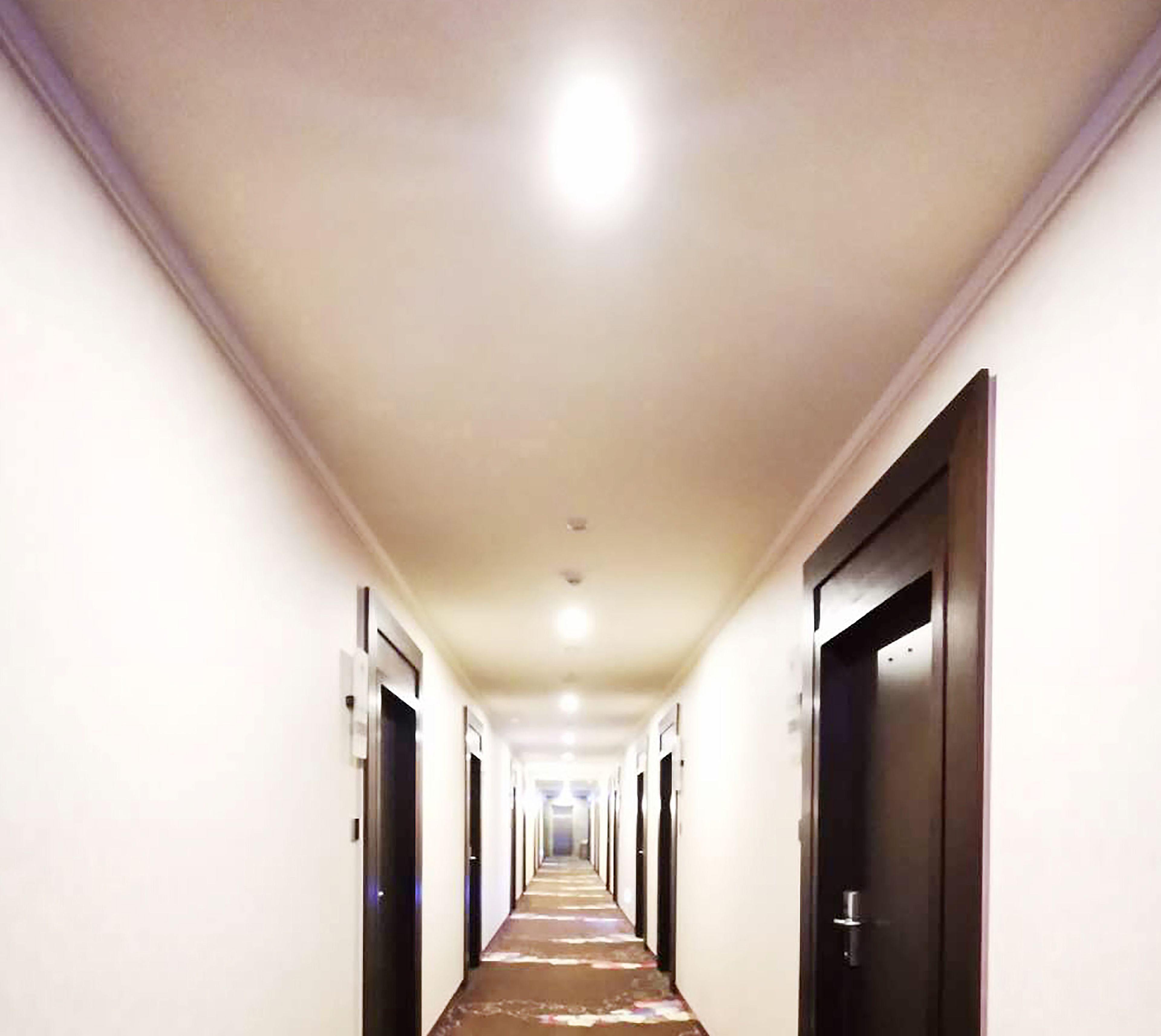 Un largo y estrecho pasillo de hotel con puertas a ambos lados, que conduce a habitaciones individuales.