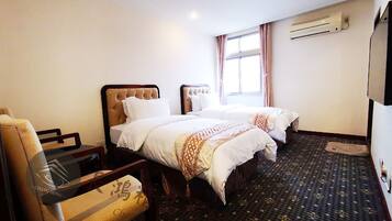 A hotel room with two beds, a chair, a small table, and an air conditioning unit on the wall.