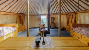 Une yourte avec des lits en bois, une table centrale ornée de tasses et d’un vase, et une vue sur l  ’extérieur.