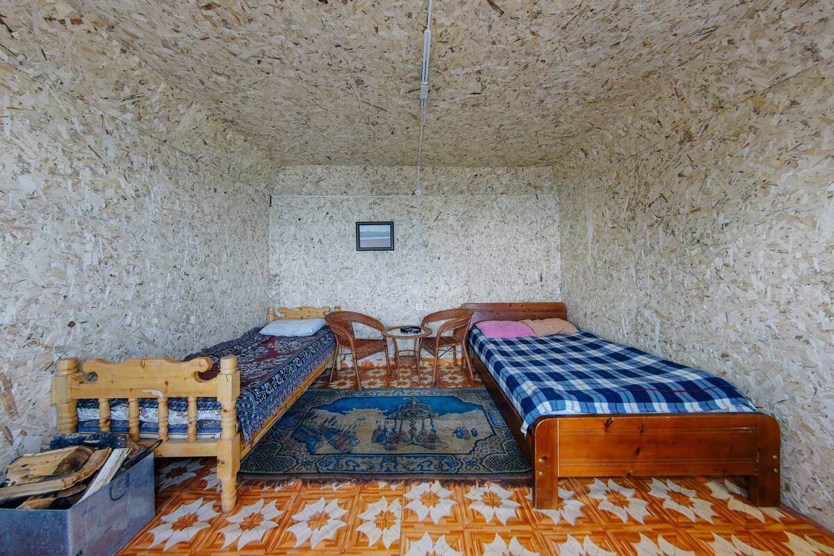 Une pièce avec deux lits en bois, une petite table avec des chaises, un tapis à motifs et un tableau accroché au mur.
